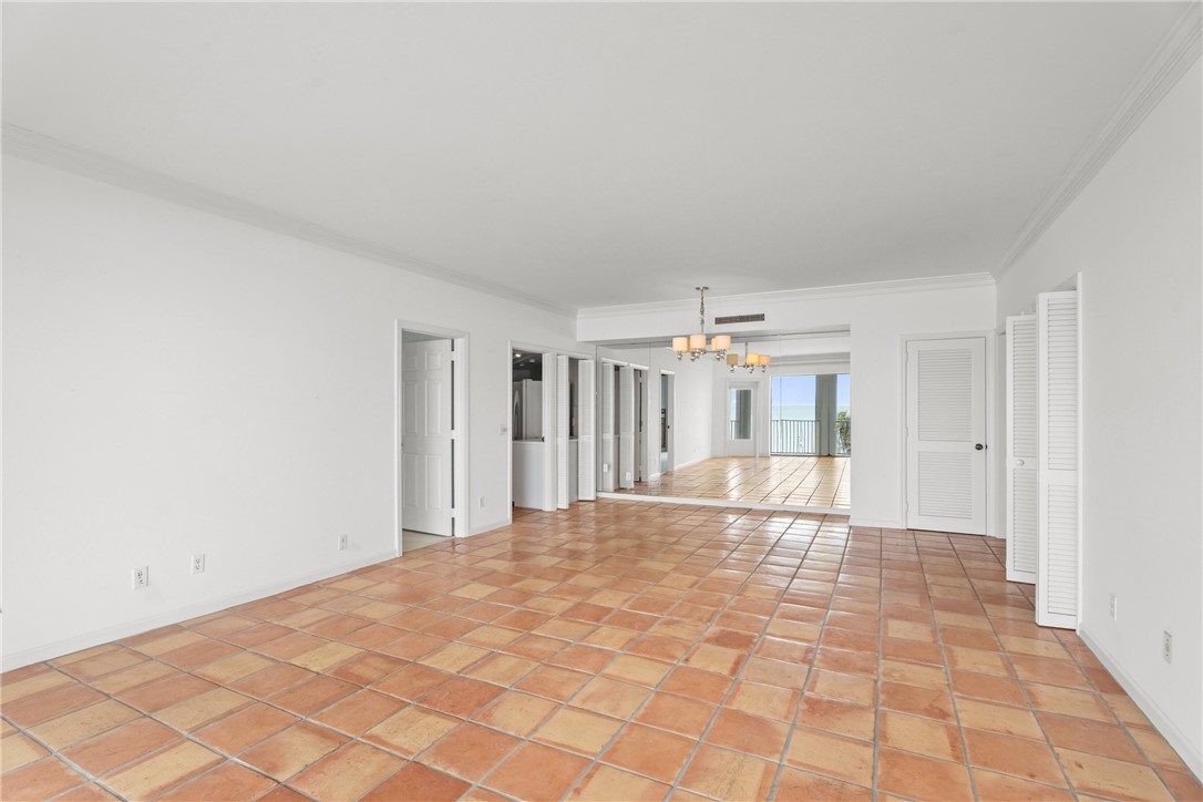 Spacious interior featuring terra cotta tile flooring, white walls, crown molding, and a chandelier