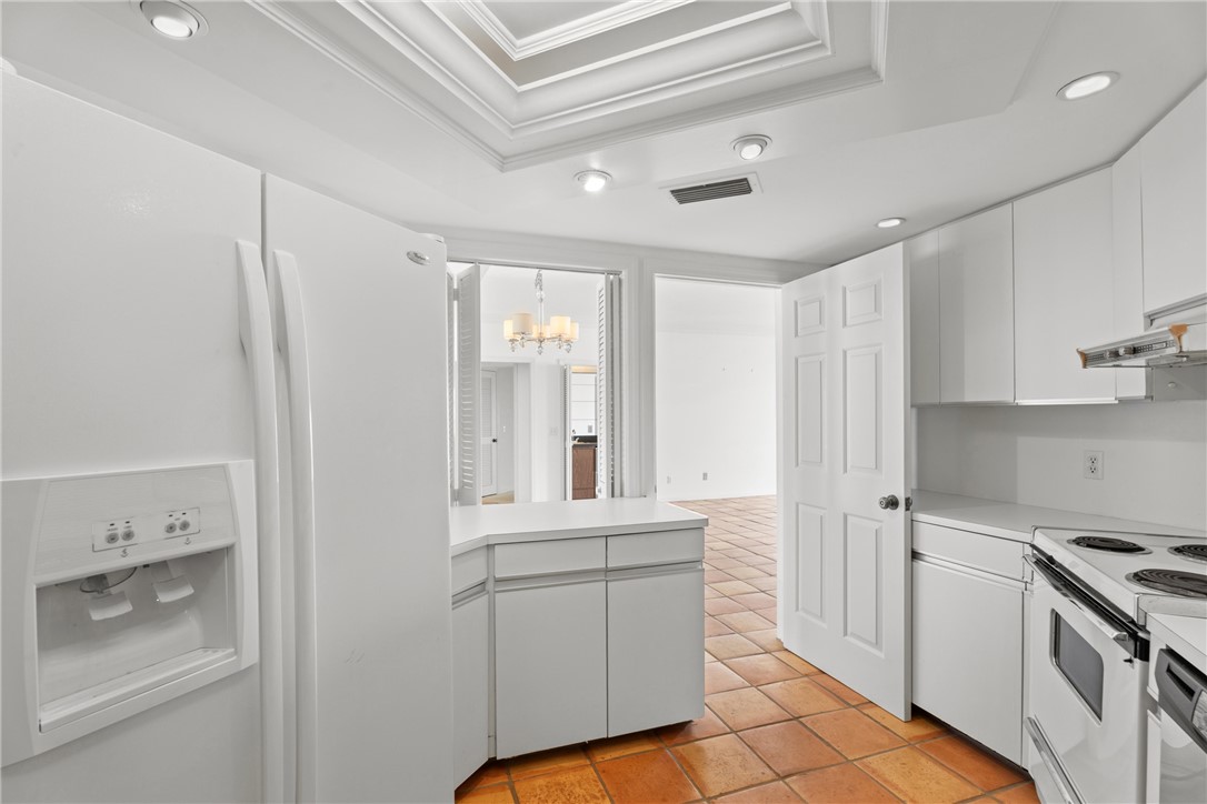 Kitchen featuring white appliances, upper and lower cabinetry, and a tiered ceiling detail