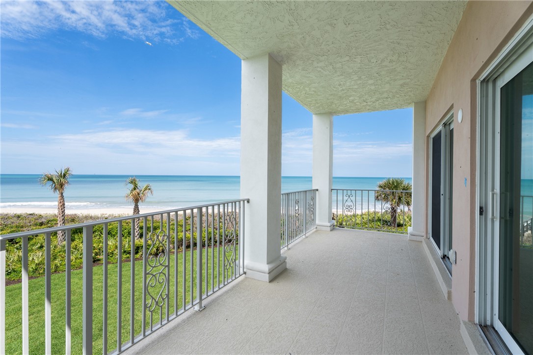 Expansive balcony featuring a textured floor, white columns, and decorative metal railings