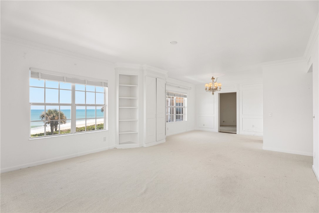 Expansive room featuring panoramic oceanfront views through large grid windows, built-in shelving, a brass chandelier, and wall panel molding