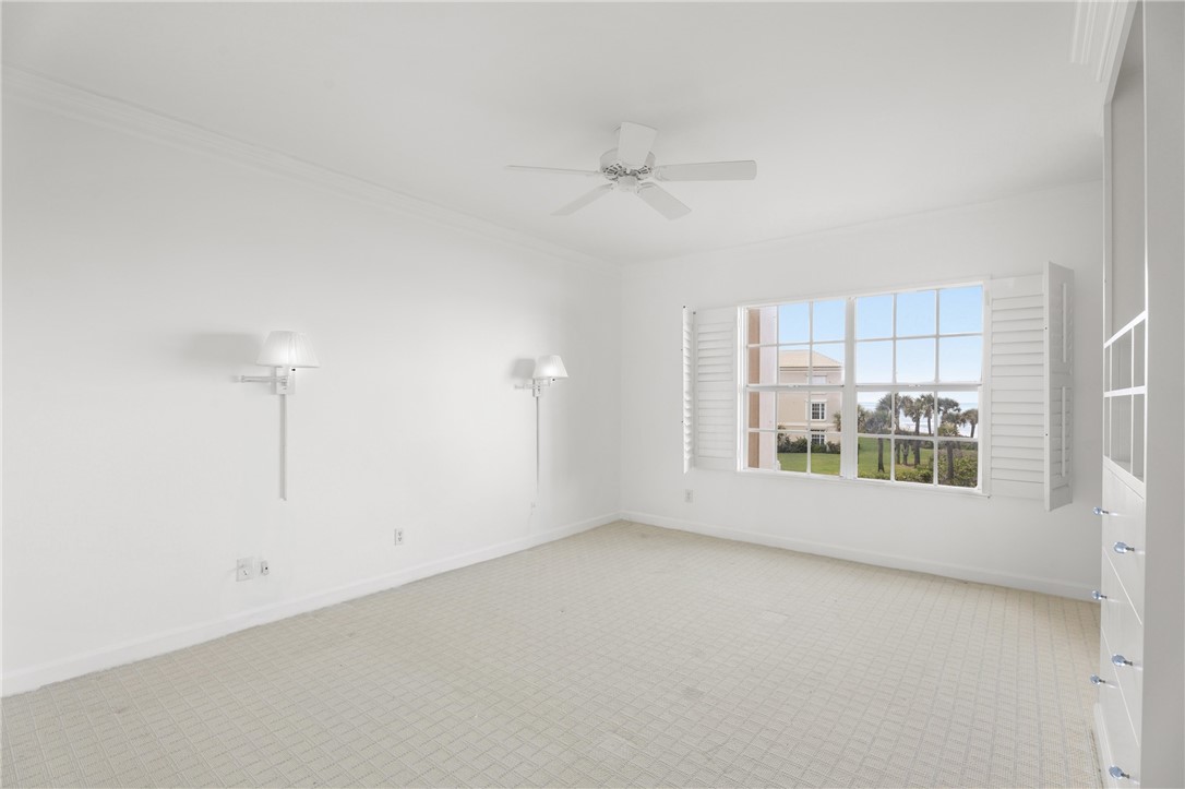 Bright interior space featuring a large window with plantation shutters, ceiling fan, crown molding, and sconce lighting