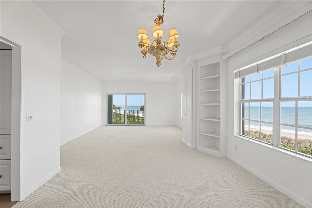 Expansive interior featuring an ornate ceiling chandelier, wall-to-wall carpeting, and floor-to-ceiling windows with direct ocean and beach scenery