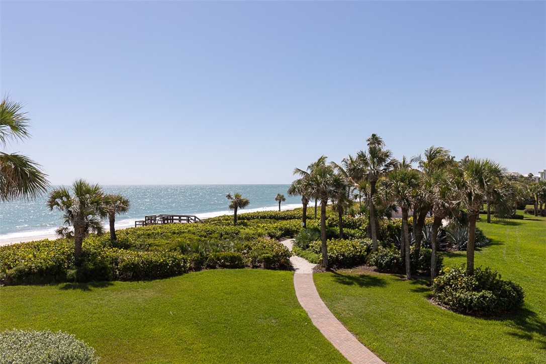 Oceanfront property featuring a sandy beach, mature palm trees, lush green landscaping, and a meandering paver pathway