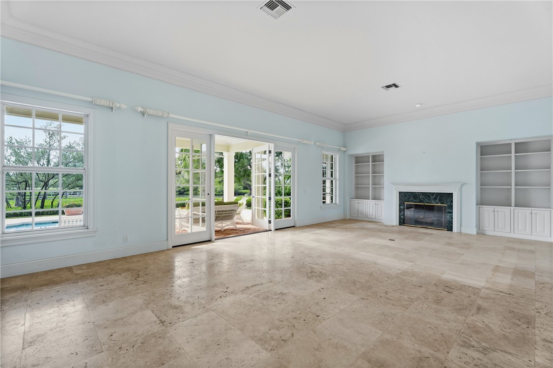 Spacious room featuring light-toned tile flooring, a fireplace with a dark stone surround, and white built-in shelving
