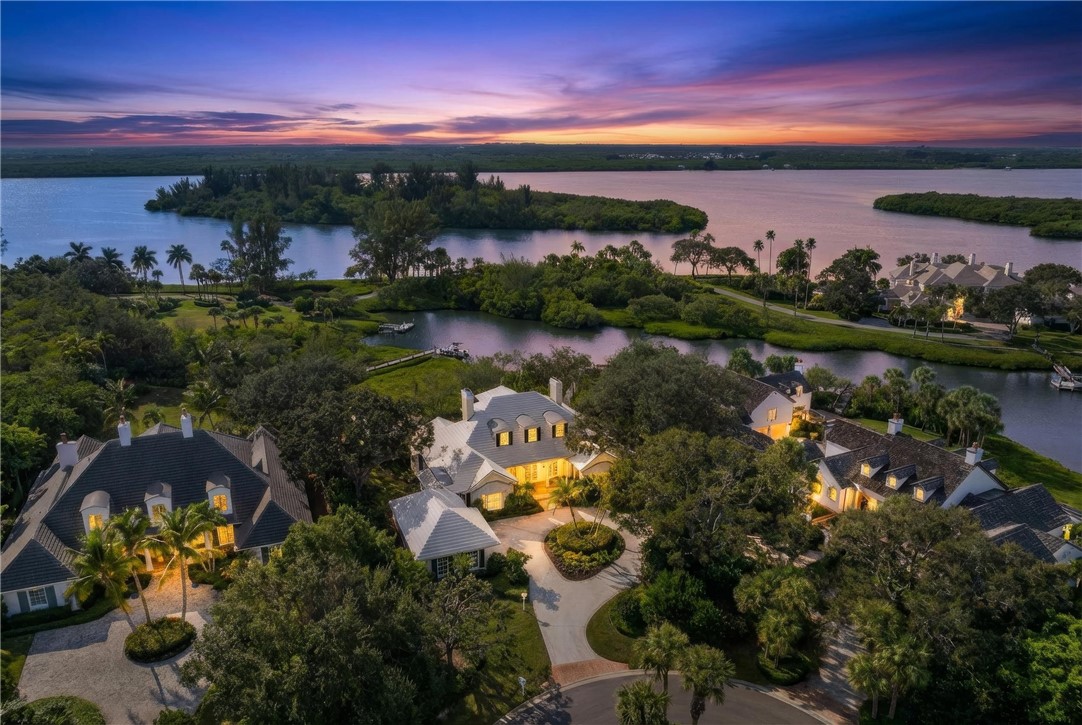 Waterfront property featuring extensive landscaping, mature trees, a private boat dock, and a paver driveway