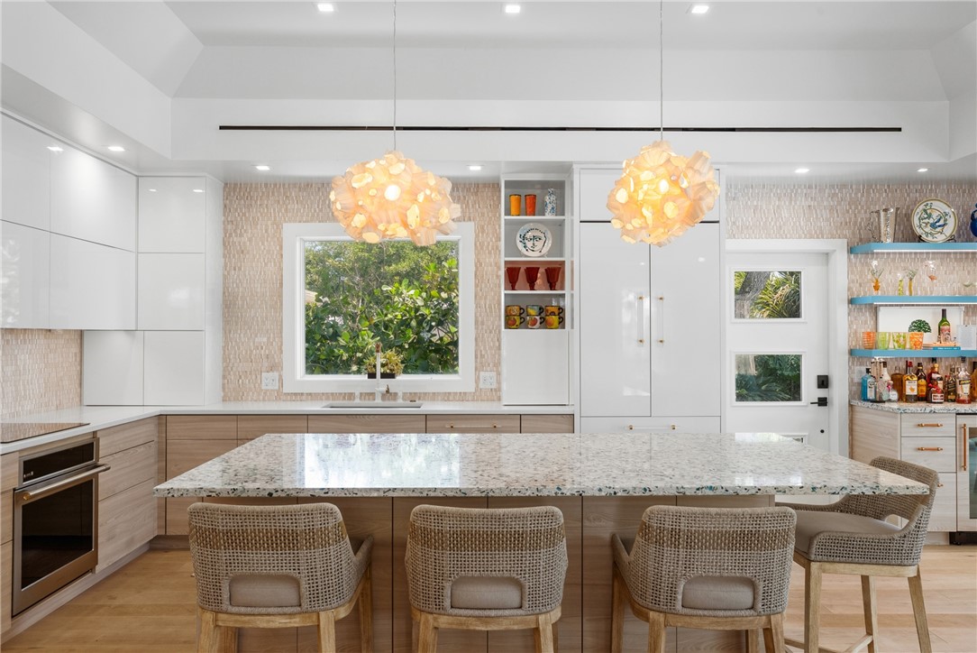 Spacious kitchen featuring a large island with seating, integrated appliances, recessed lighting, and a textured backsplash