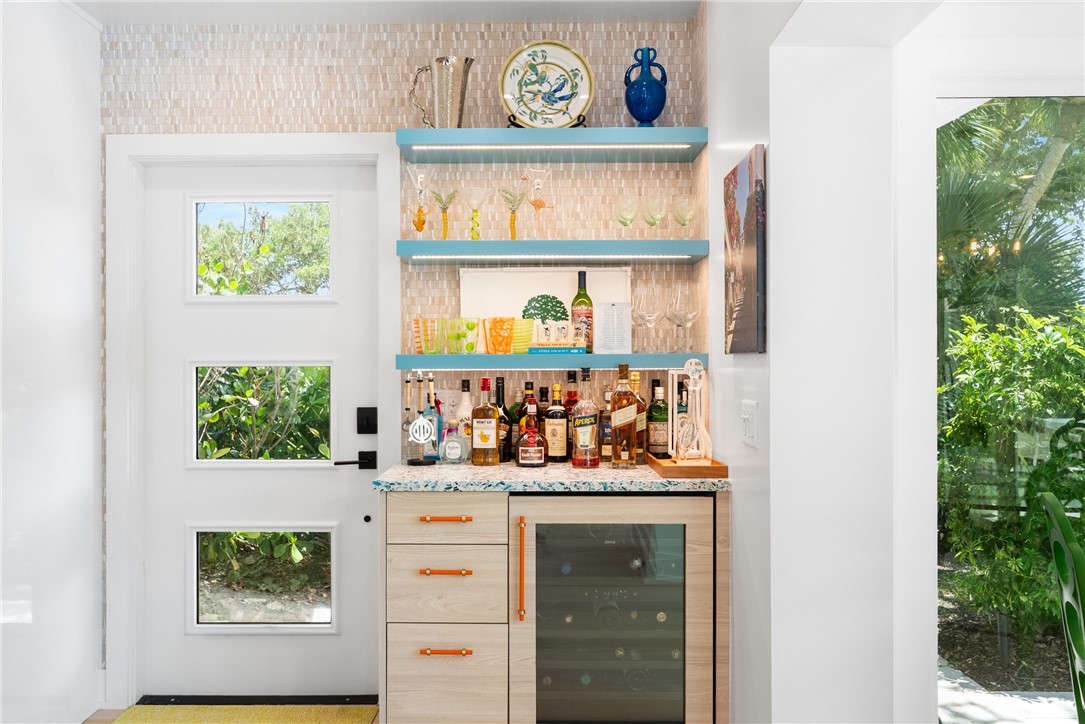 Built-in wet bar featuring a speckled countertop, integrated beverage cooler, and light wood-finish cabinetry with orange hardware