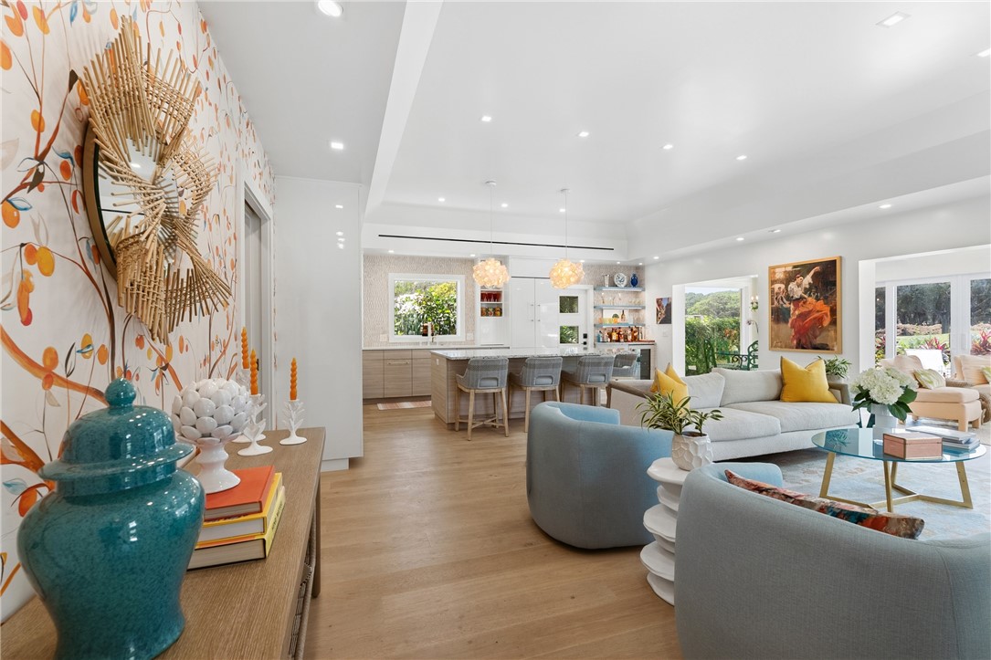 Open-concept living area featuring wood-finish flooring, a contemporary kitchen with island seating, recessed lighting, and large windows