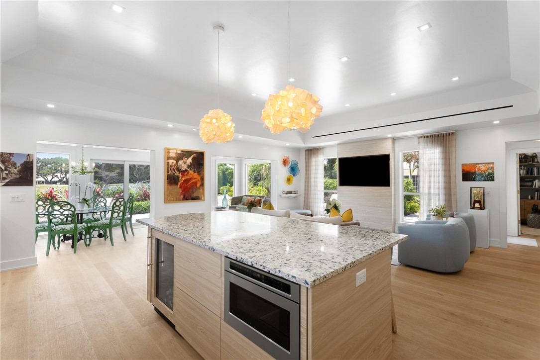 Spacious open-concept interior featuring light wood-finish flooring, a kitchen island with stone countertop, built-in microwave, and beverage cooler