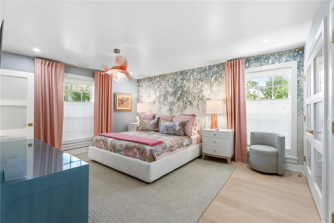 Spacious bedroom featuring light wood-finish flooring, a patterned accent wall, and a unique overhead light fixture