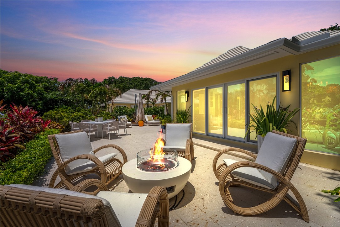 Spacious outdoor patio featuring a central fire pit, extensive paved surface, and lush perimeter landscaping
