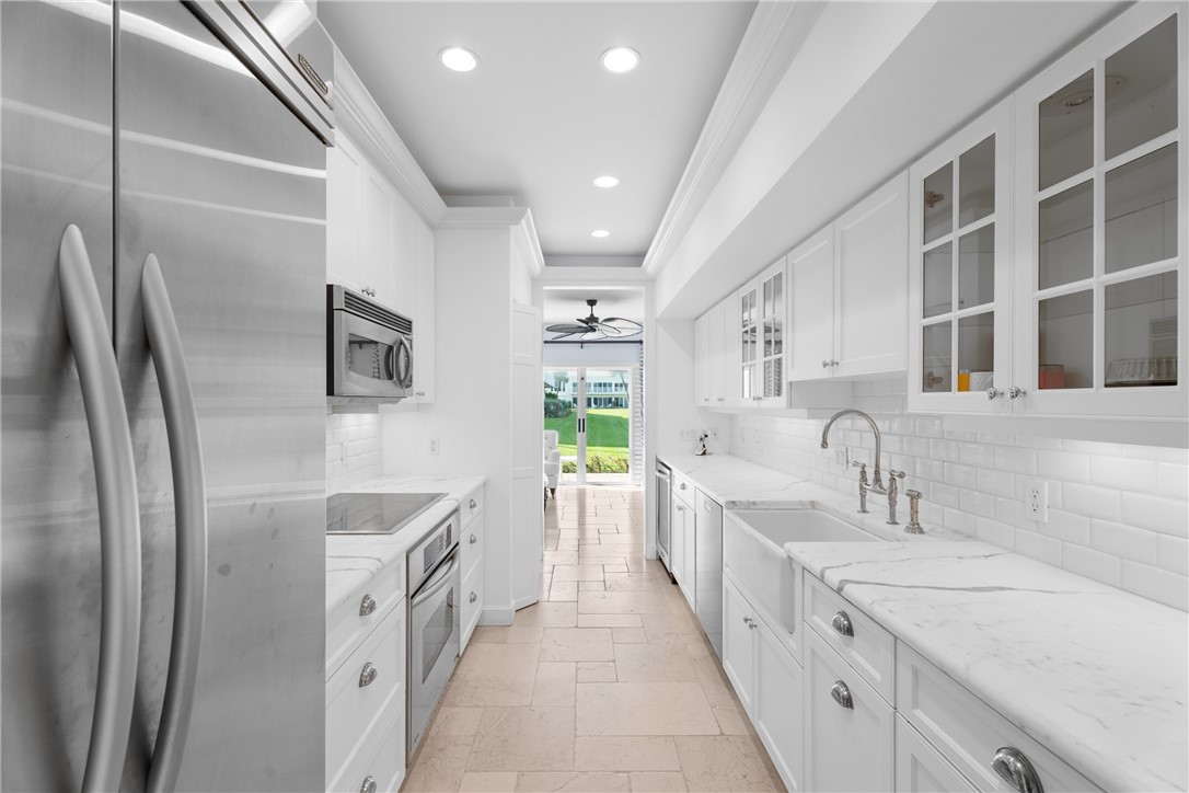 Galley kitchen featuring white cabinetry, stone countertops, integrated sink, stainless steel appliances, and recessed lighting