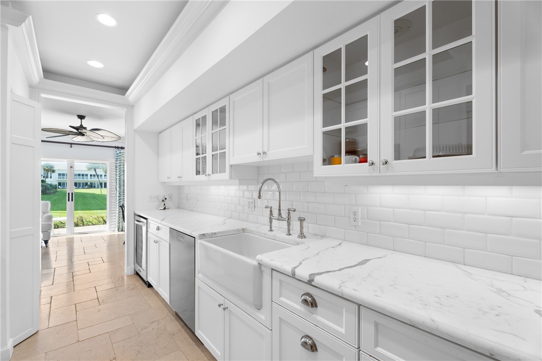 Kitchen featuring white cabinetry, subway tile backsplash, white countertops with natural veining, a farmhouse sink with a gooseneck faucet, and integrated stainless steel appliances