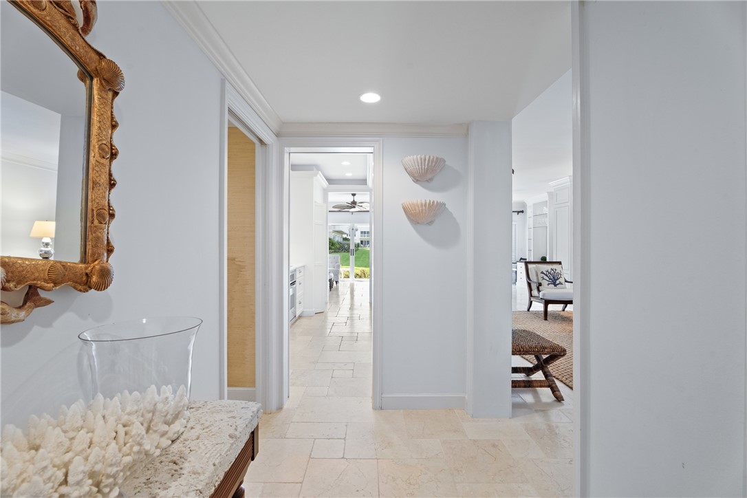 Hallway featuring a decorative mirror, neutral wall sconces, and light-toned tile flooring