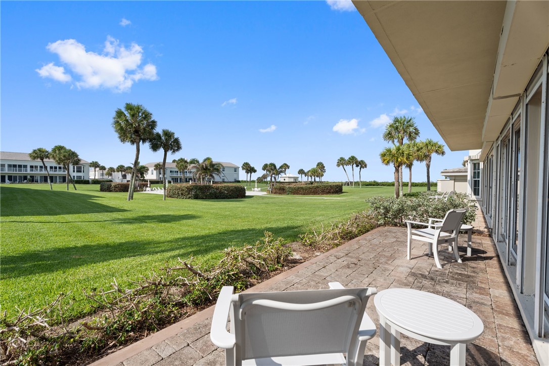 Patio area featuring paver flooring, extensive green lawn, mature palm trees, and distant water