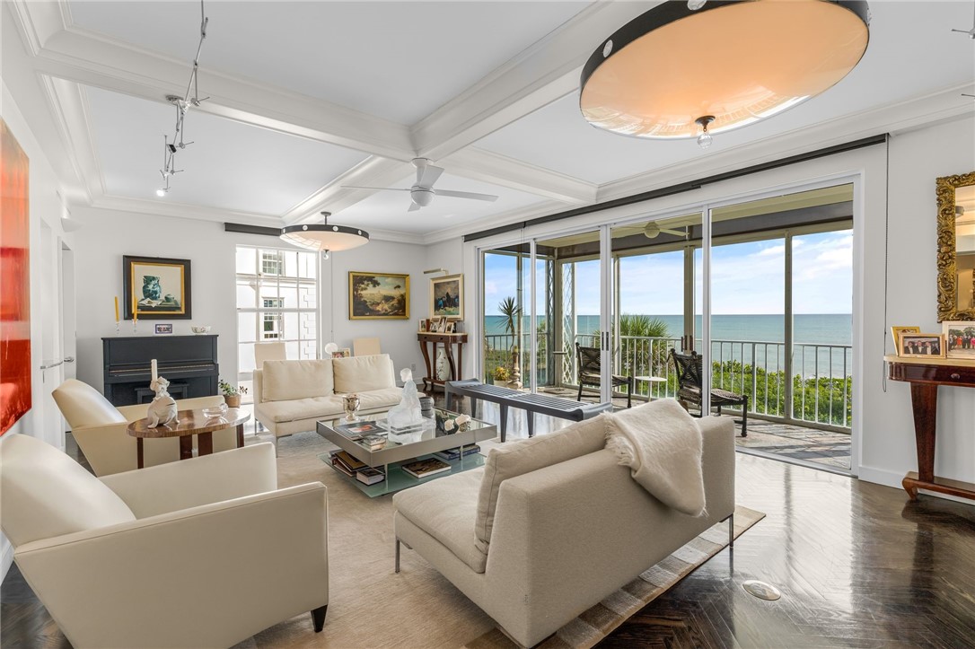 Spacious living area featuring coffered ceilings, dark wood-finish flooring, and a screened balcony overlooking the ocean