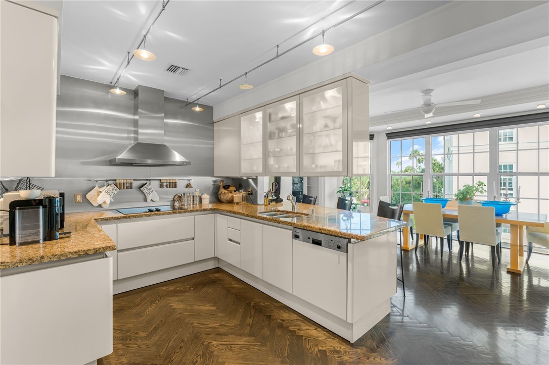Modern kitchen featuring light-toned cabinetry, granite countertops, stainless steel appliances, and wood-finish herringbone flooring