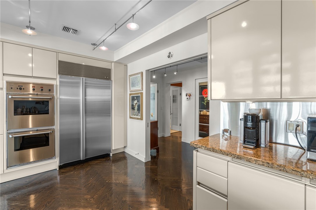 Kitchen featuring high-gloss cabinetry, stainless steel double ovens, a built-in stainless steel refrigerator, granite countertops, and wood-finish flooring