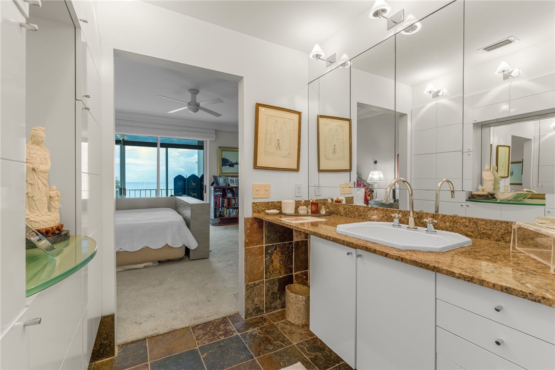 Guest bathroom featuring dual vanities with warm-toned stone countertops, white cabinetry with ample storage