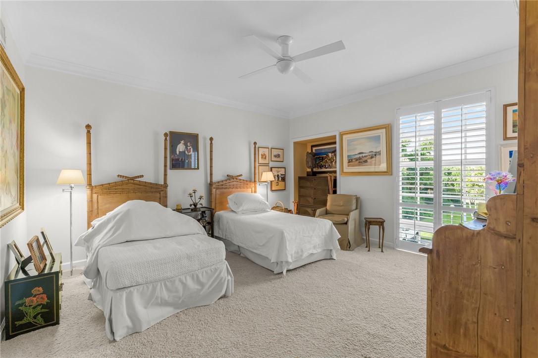 Spacious guest bedroom with ceiling fan, carpeted flooring, and abundant natural light from shuttered glass doors