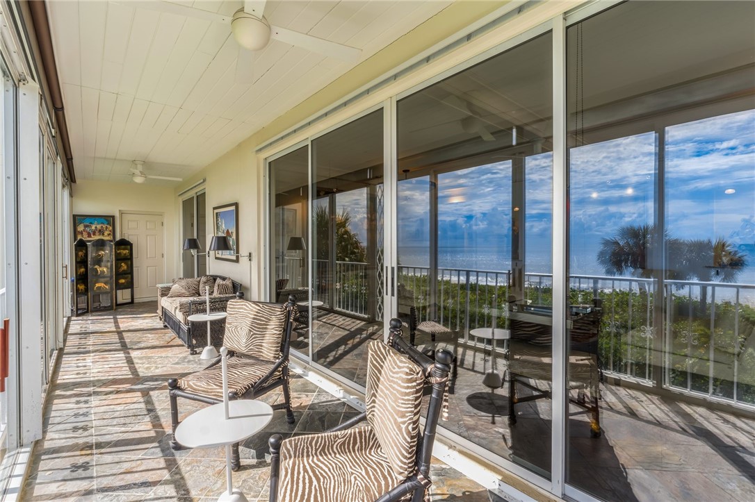 Expansive enclosed porch with panoramic water views, featuring multiple sets of sliding glass doors, wood-finish flooring, and ceiling fans