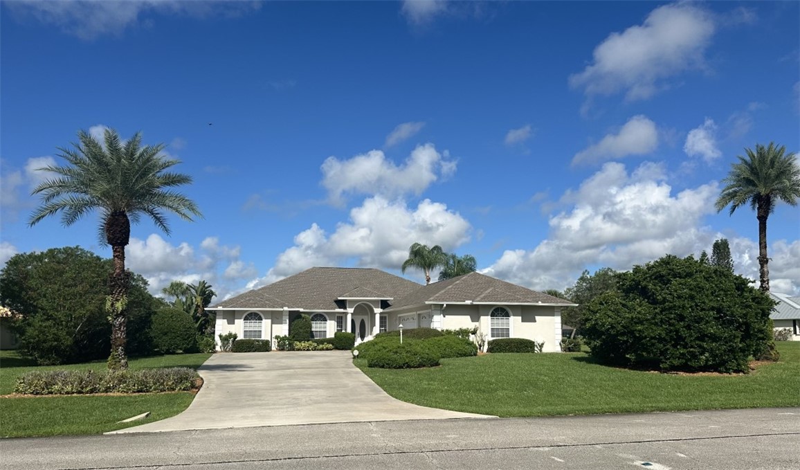 Expansive front lawn with mature landscaping, a concrete driveway, and a white exterior facade