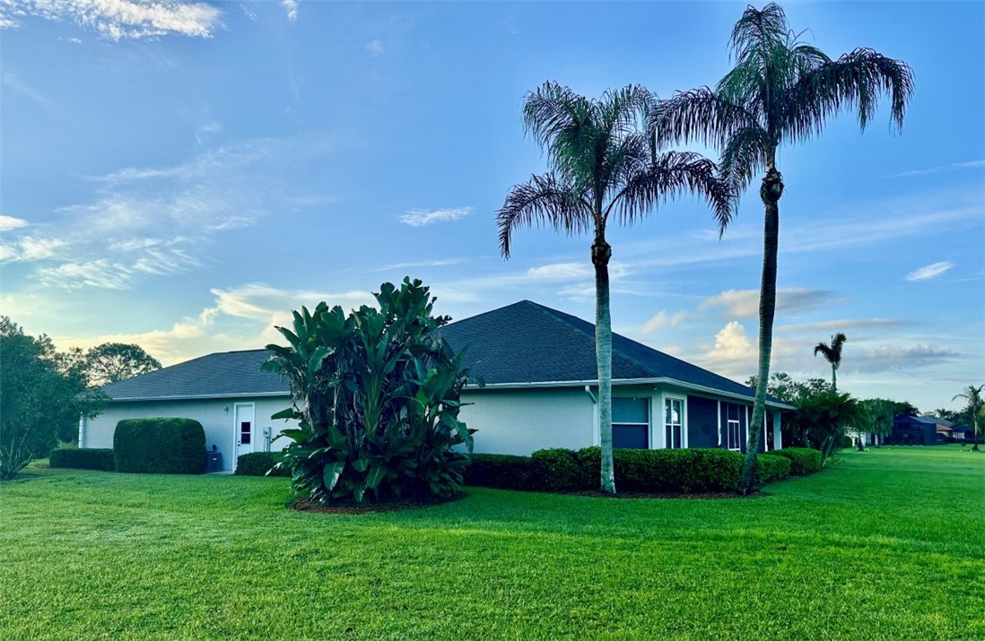 Expansive lawn with mature palm trees, featuring a stucco exterior and a screened patio