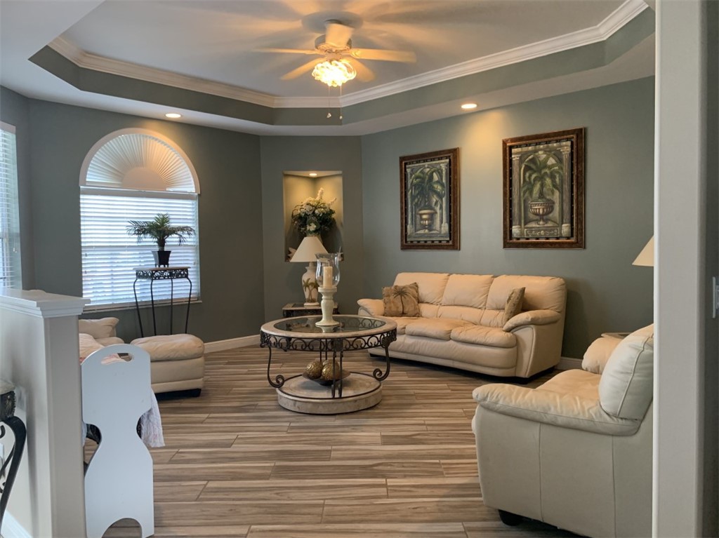 Tray ceiling with crown molding, recessed lighting, wood-finish flooring, built-in wall niche, and an arched window
