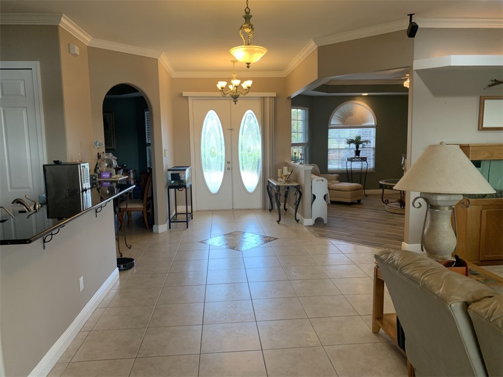 Tile flooring with an accent inlay, double entry doors with decorative glass, arched doorways, crown molding, and a built-in breakfast bar with a dark countertop
