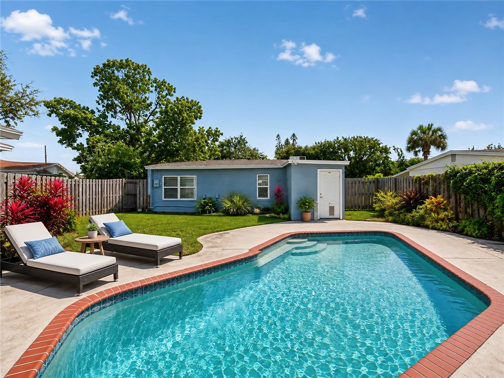 In-ground swimming pool with brick coping, concrete pool deck, and a detached structure with a white exterior door