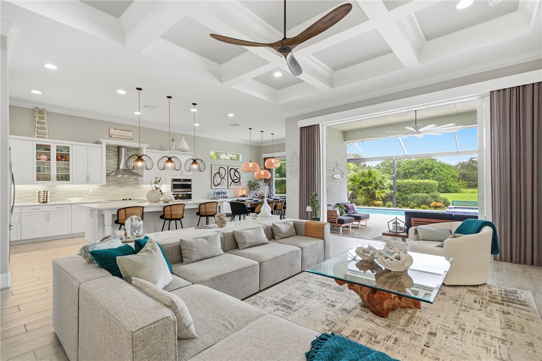 Coffered ceiling with a ceiling fan, spacious open concept living area, kitchen island with seating, built-in kitchen appliances, and large sliding glass doors opening to a screened patio and swimming pool
