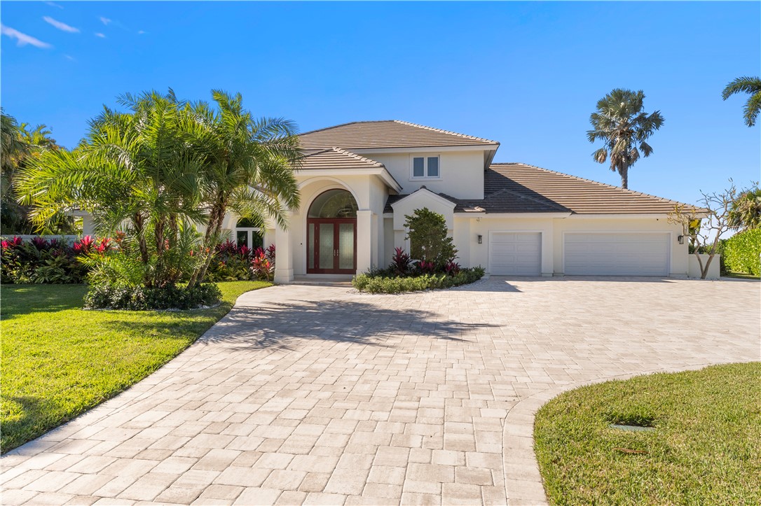 Mediterranean-inspired residence featuring a stucco exterior with arched entryway, dual three-car garage with matching architectural detailing, and a sweeping paver driveway