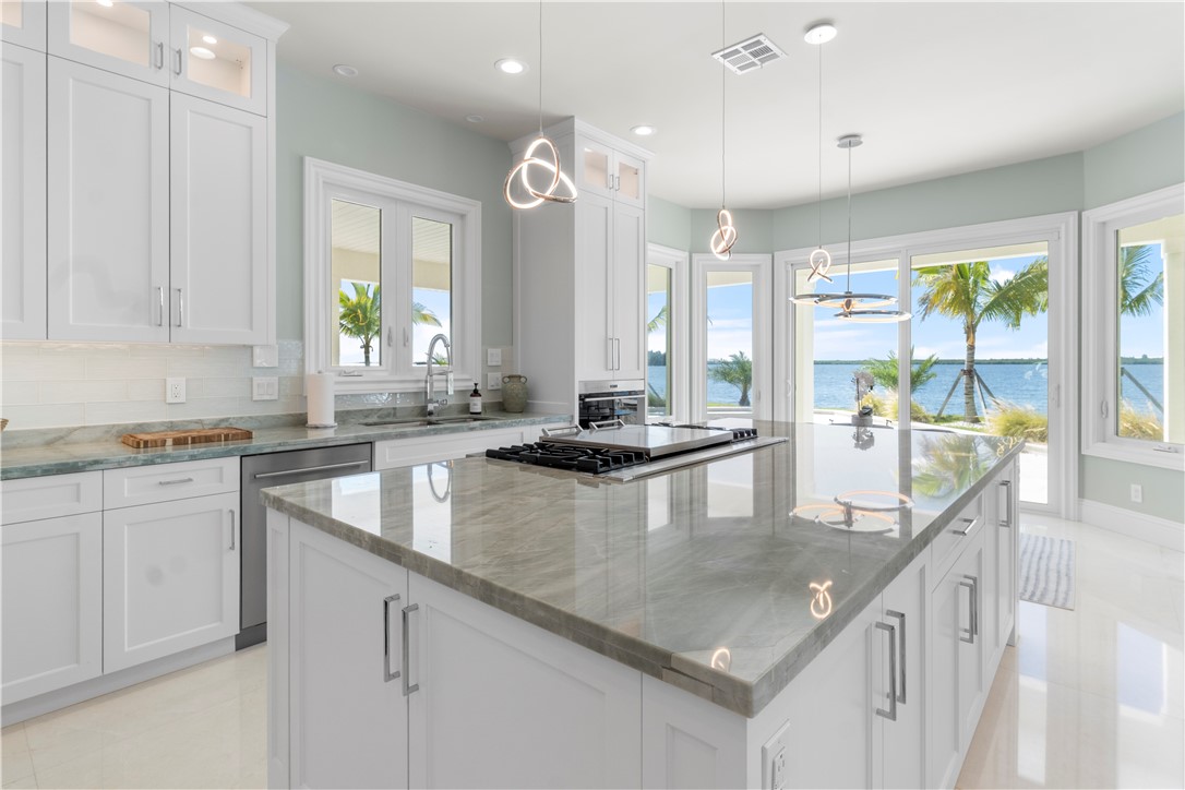 Gourmet kitchen with an expansive island, integrated cooktop, white shaker cabinetry, and a full suite of stainless steel appliances