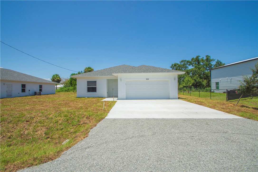 Newly constructed home featuring a clean-lined architectural design with a pitched roof, wide driveway with concrete surface, and an expansive front lawn