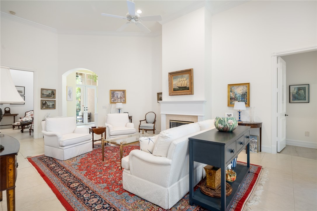 Vaulted ceiling with a ceiling fan, fireplace with a mantel, arched window, and tile flooring
