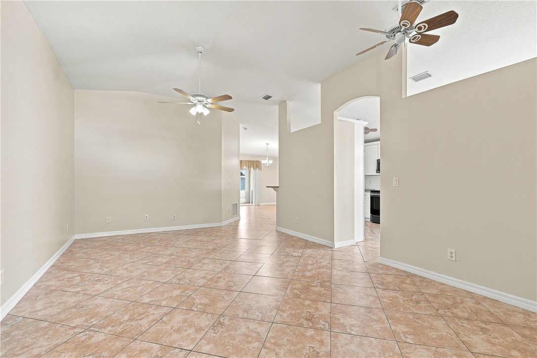 Spacious open-concept living area featuring tile flooring, vaulted ceilings with ceiling fans, abundant natural light from skylights, and a central column defining the layout
