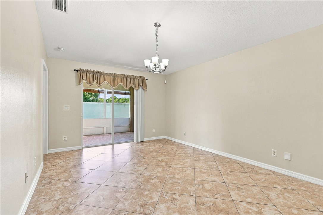 Spacious dining area featuring neutral-toned walls, tile flooring with stone-finish detail, and glass sliding doors opening to outdoor space