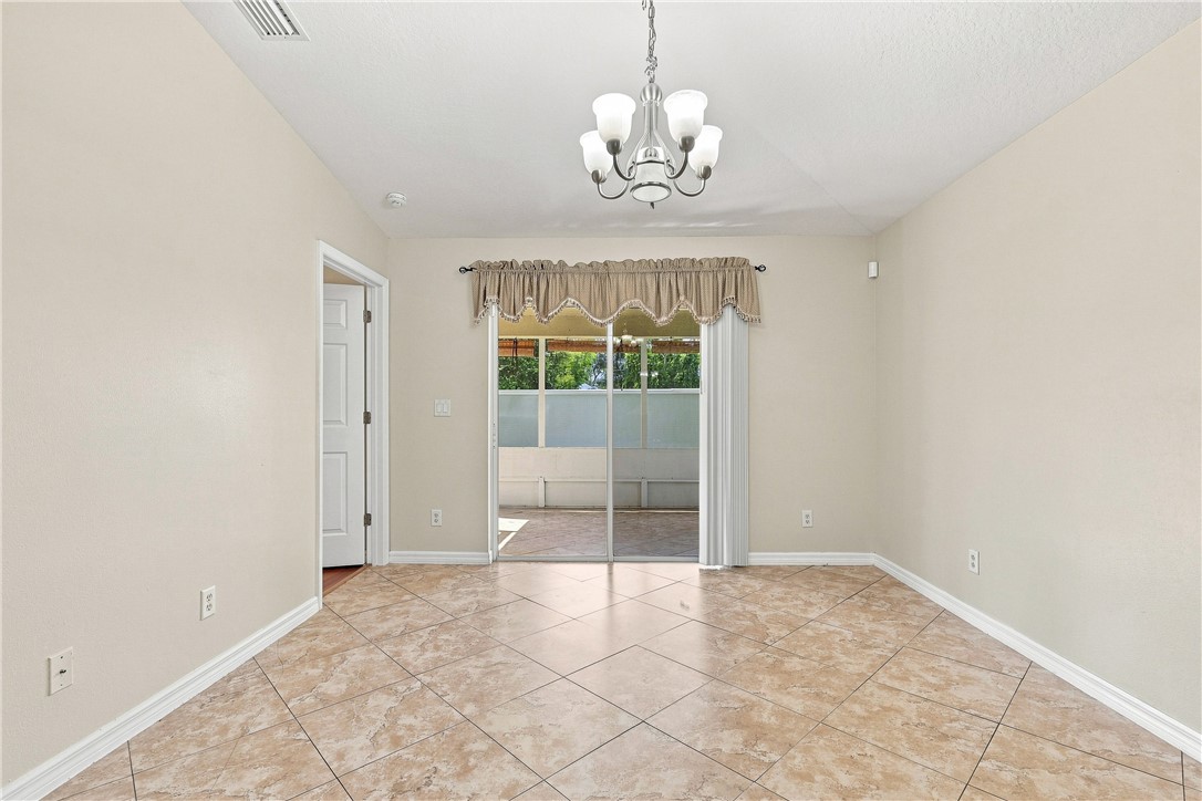 Bright and spacious room featuring tile flooring, a glass sliding door with transom windows, elegant chandelier lighting, and neutral wall finishes throughout