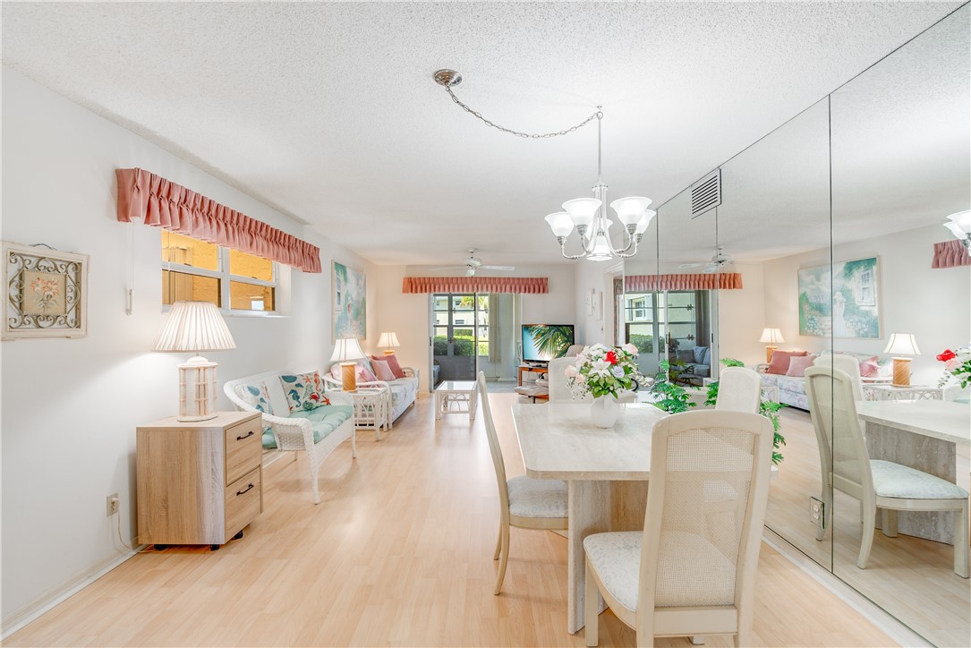 Open living and dining areas featuring wood-finish flooring, a wall of mirrors, and a multi-light chandelier