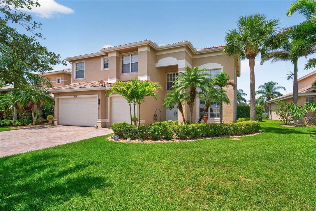 Two-story residence featuring a terracotta tile roof, two garage doors, a paver driveway, and a manicured lawn with mature palm trees