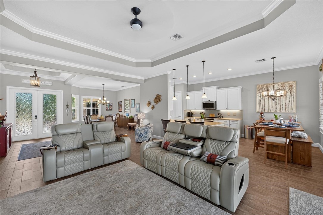 Open-concept living area featuring tray ceilings, wood-finish flooring, and recessed lighting