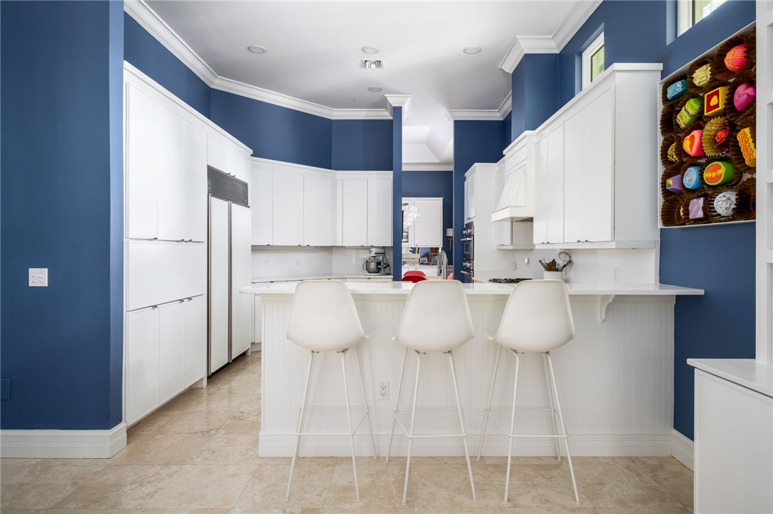 Renovated kitchen featuring extensive white cabinetry, an integrated refrigerator, a center island, peninsular with bar seating, a built-in range hood, and tile flooring