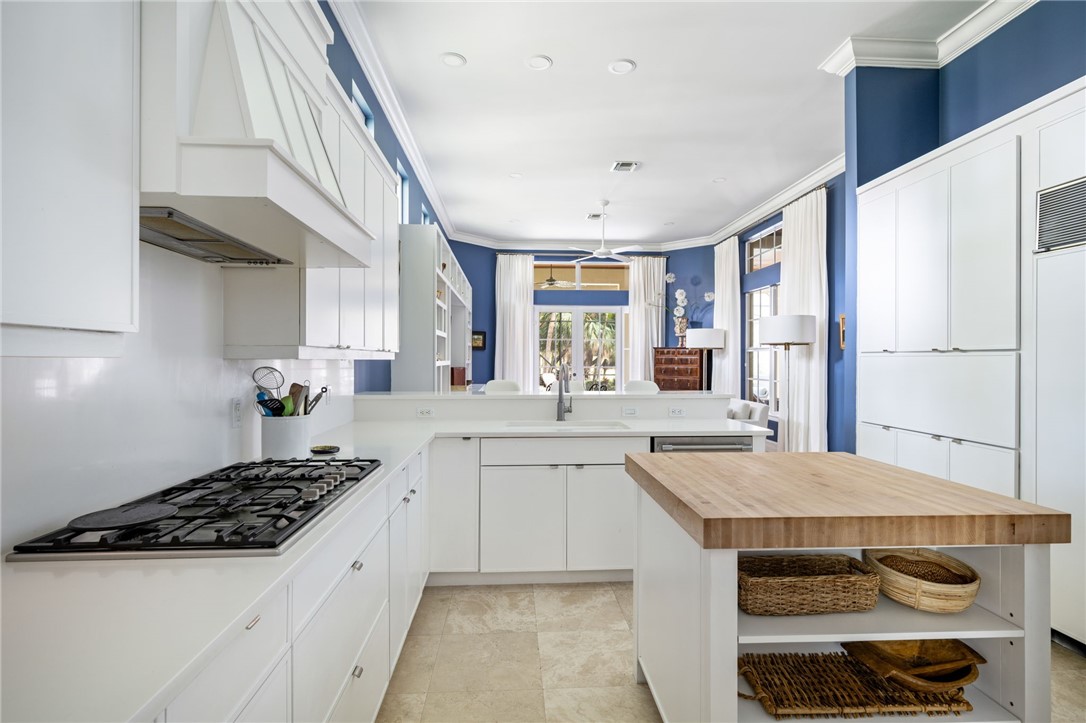White cabinetry with chrome hardware, U-shaped kitchen with built-in gas range, wood-top center island, and recessed lighting
