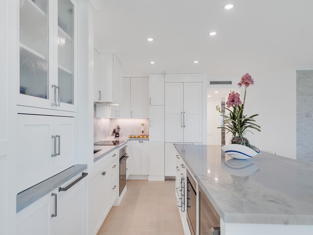 White cabinetry, recessed ceiling lighting, light-toned flooring, integrated refrigerator, and a kitchen island with a stone surface