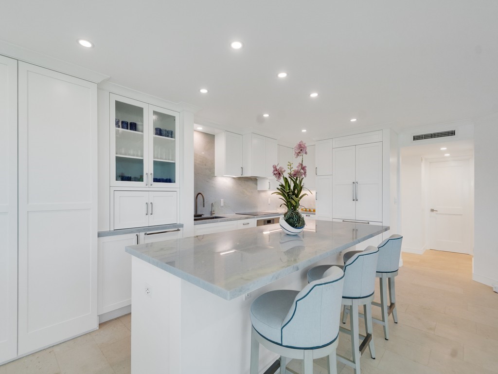 White cabinetry, built-in appliances, glass-front upper cabinets, light-toned flooring, and recessed lighting