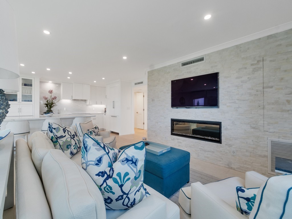 Recessed lighting, integrated linear fireplace, stone-finish accent wall, white cabinetry with glass-front uppers, and light-toned flooring