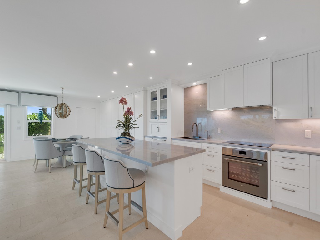 Open-concept kitchen with a large central island, white cabinetry, integrated stainless steel oven, and light-toned tile flooring