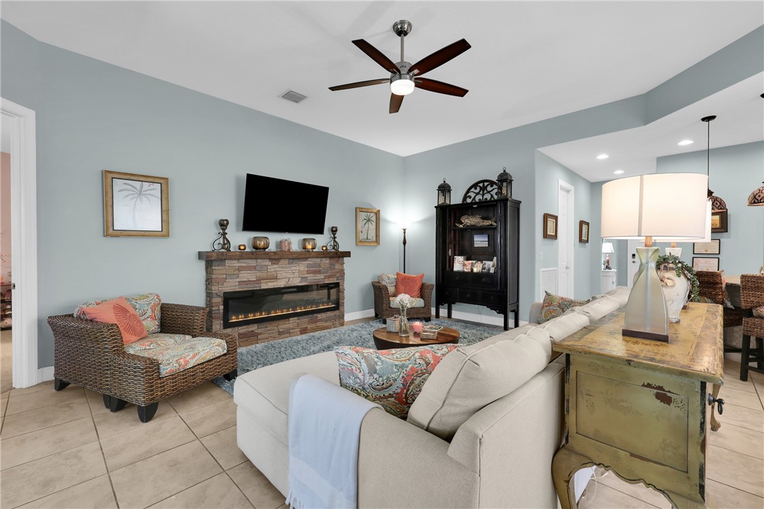 Living space featuring a stacked stone fireplace with an integrated electric insert, a ceiling fan with light, recessed lighting, and tile flooring