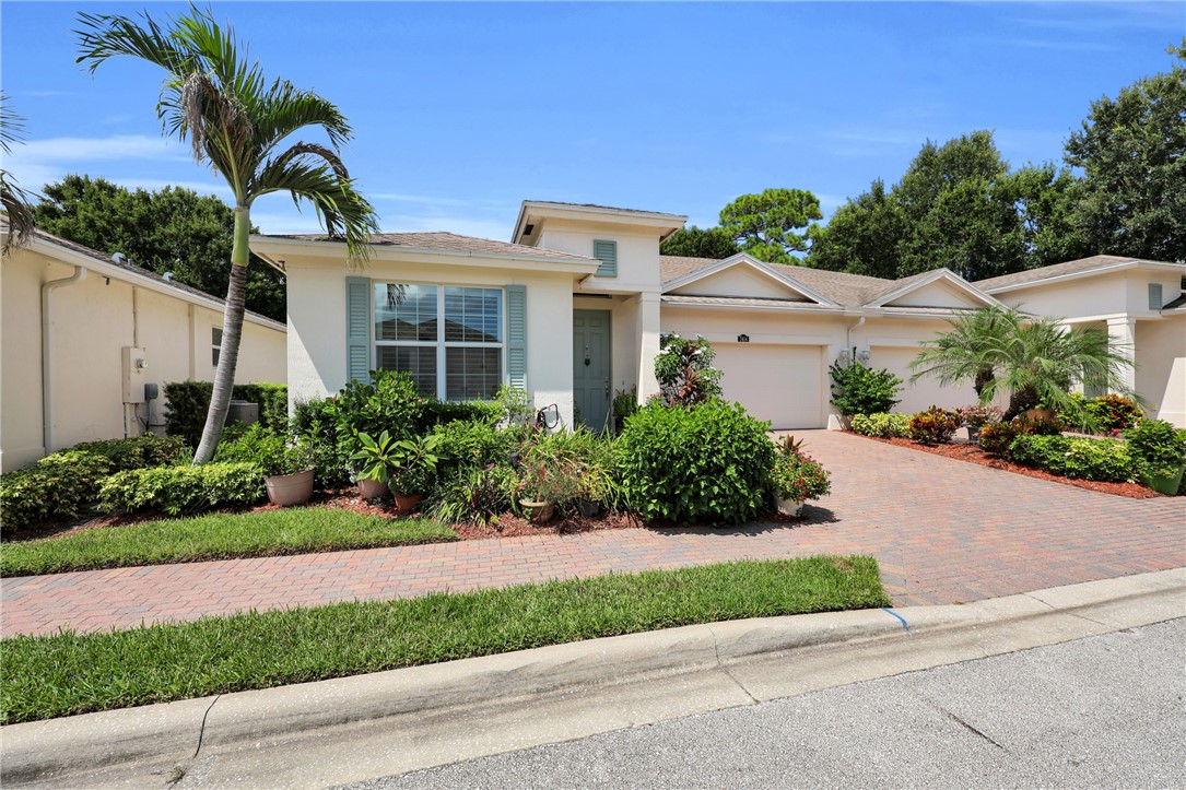 Stucco exterior with a tiled roof, featuring a brick paver driveway and a lushly landscaped front yard