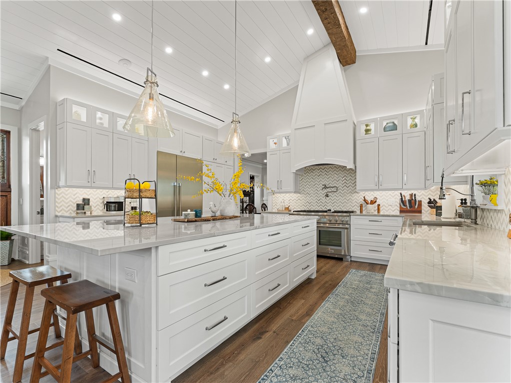 Gourmet kitchen featuring a substantial island with stone countertops, integrated stainless-steel appliances, white cabinetry, a herringbone tile backsplash, and wood-finish flooring